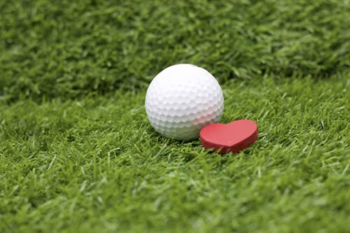 A golf ball with a heart next to it on grass