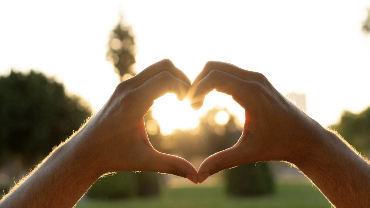 Two hands forming a heart with the sun in the background